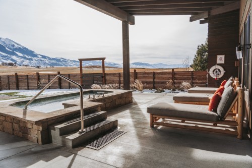 A serene outdoor space with lounge chairs, a hot tub, and mountain views under a clear sky.