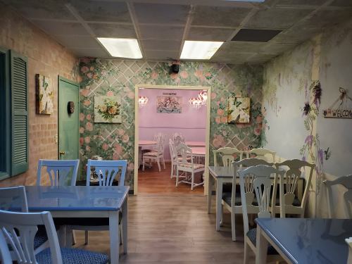 Cozy café interior with floral wallpaper, white tables, and chairs, leading to a welcoming dining area.