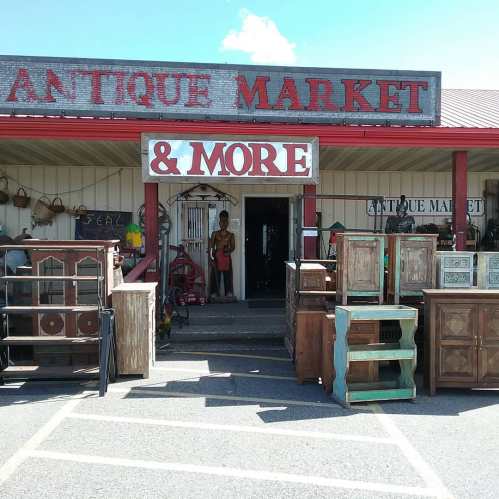 A rustic antique market with wooden furniture outside and a person standing near the entrance. Bright blue sky above.