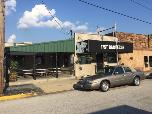 Exterior of 17th Barbecue restaurant with a green awning, outdoor seating, and a parked car in front.