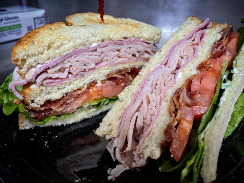 A close-up of a sandwich with layers of turkey, bacon, lettuce, and tomato, served on toasted bread.