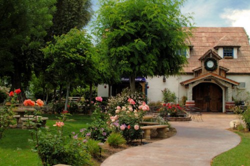 A charming garden path leads to a quaint cottage surrounded by lush greenery and colorful rose bushes.