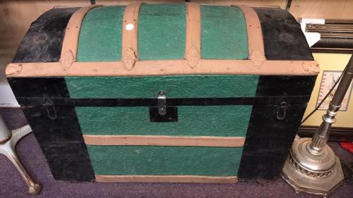 A vintage trunk with a green and black exterior, featuring leather straps and a central lock.
