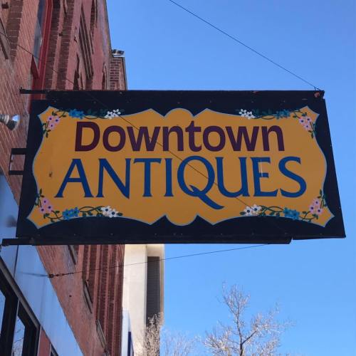 Sign for "Downtown Antiques" against a clear blue sky, with decorative elements in yellow and blue.