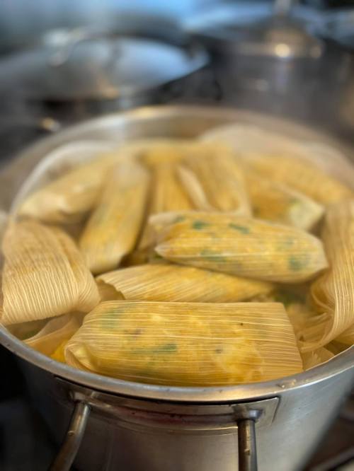 A pot filled with steaming tamales wrapped in corn husks, ready to be served.