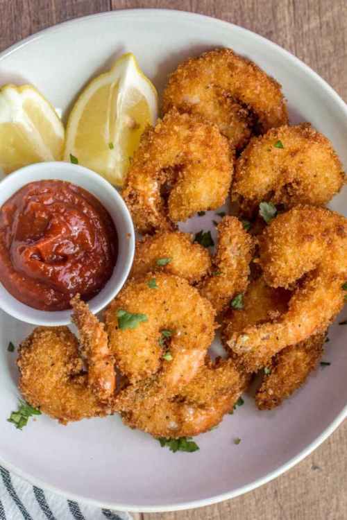 A plate of crispy fried shrimp with a side of marinara sauce and lemon wedges, garnished with parsley.
