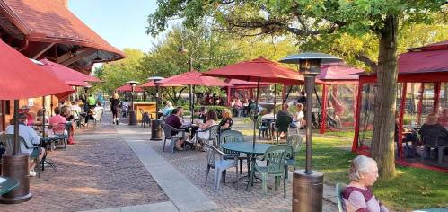 Outdoor seating area with green chairs and red umbrellas, filled with people enjoying the pleasant weather.