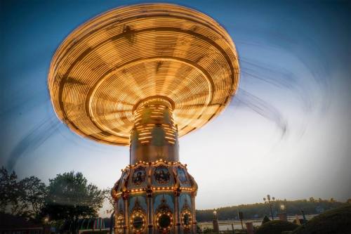A brightly lit carousel spinning against a twilight sky, creating a sense of motion and excitement.