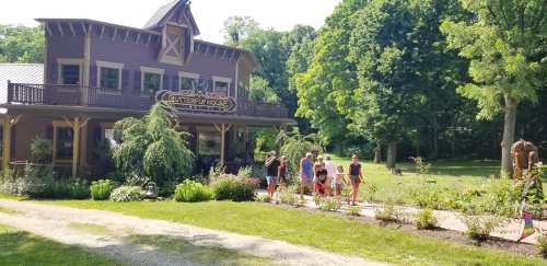 A charming building surrounded by greenery, with people walking along a path in a sunny outdoor setting.