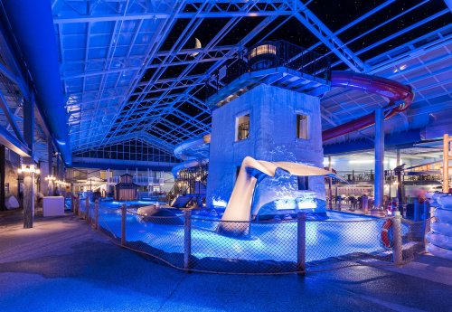 Indoor water park featuring a lighthouse structure, water slides, and blue lighting, creating a fun, aquatic atmosphere.