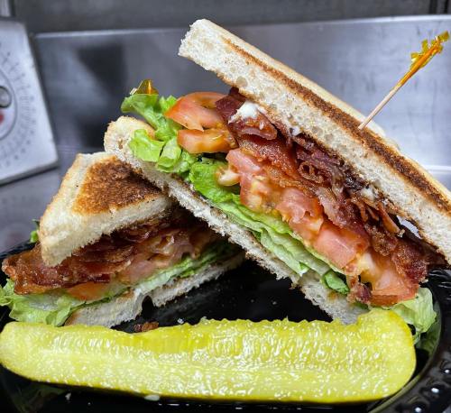 A toasted sandwich with bacon, lettuce, and tomato, served with a pickle on the side.