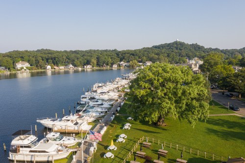 A serene lakeside view with boats docked, green trees, and a clear sky, creating a peaceful atmosphere.