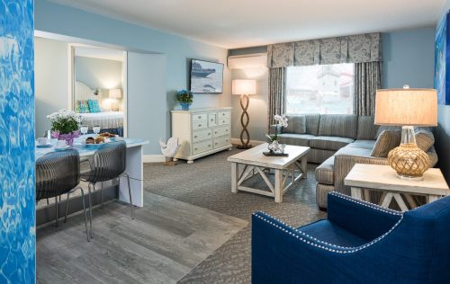A cozy hotel suite featuring a living area with a sofa, coffee table, and dining space, decorated in light colors.