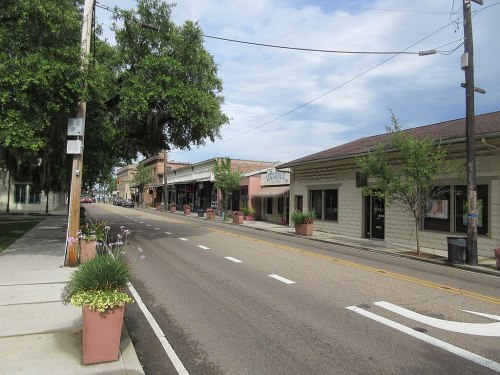 A quiet street lined with shops and planters, featuring trees and a cloudy sky overhead.