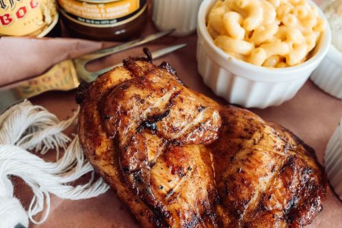 Grilled chicken breast served with macaroni and cheese, alongside barbecue sauces on a rustic table setting.