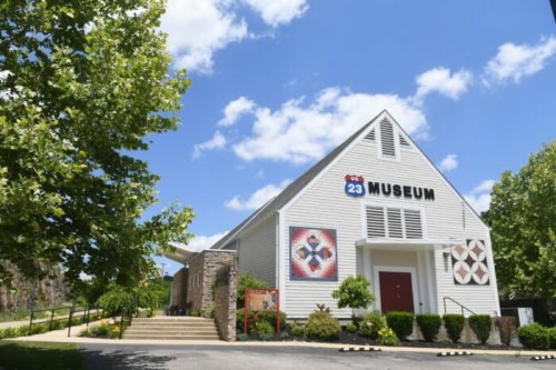 A white museum building with a blue sky and fluffy clouds, surrounded by greenery and steps leading to the entrance.
