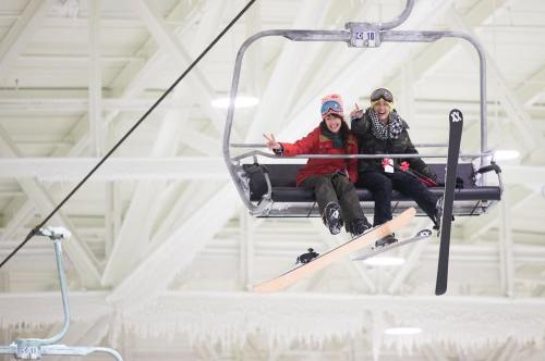 Two friends on a ski lift, smiling and making peace signs, with snowboards beside them in a winter setting.
