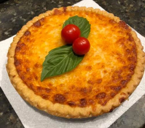 A golden-brown pie topped with two cherry tomatoes and fresh basil leaves, resting on a paper napkin.