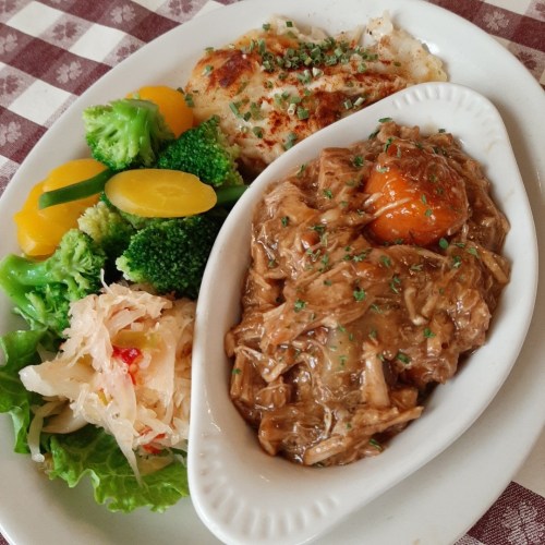 A plate featuring shredded meat with an egg, sautéed vegetables, and a side of sauerkraut on a checkered tablecloth.