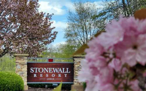 Sign for Stonewall Resort Lodge surrounded by blooming flowers and trees under a blue sky.