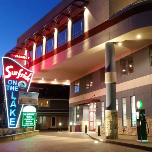 Neon sign for Surfside on the Lake hotel at dusk, showcasing "Vacancy" and amenities, with modern architecture in the background.