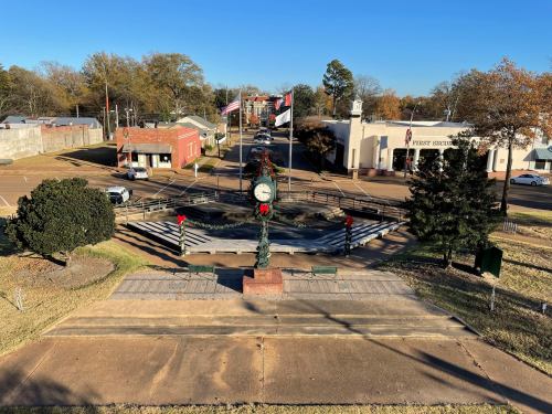 A clock tower adorned with holiday decorations overlooks a small town street lined with buildings and flags.