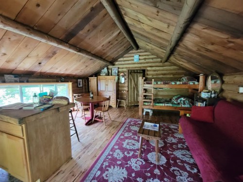 Cozy wooden cabin interior with a dining table, bunk beds, and a red sofa, featuring rustic decor and natural light.