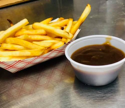 A serving of golden French fries in a basket next to a small cup of brown gravy.