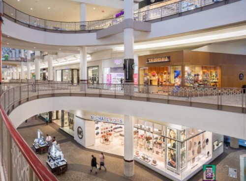 A spacious mall interior with multiple levels, featuring stores like Michael Kors and Teavana, and open walkways.