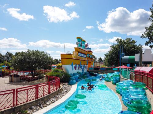 A colorful water park with a lazy river, floating tubes, and a large ship structure in the background under a blue sky.