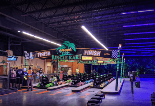 Indoor go-kart track with vibrant jungle-themed decor, featuring karts lined up and a finish line sign.