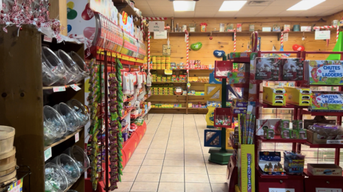 A colorful candy store aisle filled with various sweets, jars, and games, creating a festive atmosphere.
