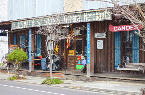 A rustic general store with wooden exterior, vintage signs, and canoes displayed outside.