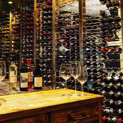 A wine cellar featuring a wooden table with glasses and bottles, surrounded by racks filled with various wines.