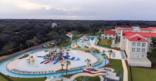 Aerial view of a colorful water park with slides, pools, and lush greenery surrounding a large building.