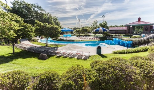 A sunny pool area with lounge chairs, umbrellas, and lush greenery surrounding the water.