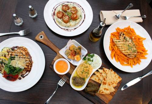 A table set with four dishes: pasta, grilled chicken, appetizers, and risotto, garnished and elegantly presented.