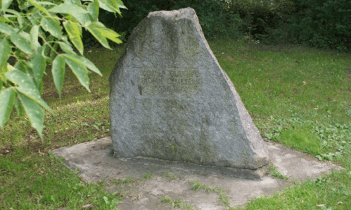 A large, weathered stone monument stands on a grassy area, partially surrounded by trees.