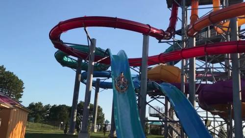 A person slides down a colorful water slide at a water park on a sunny day.