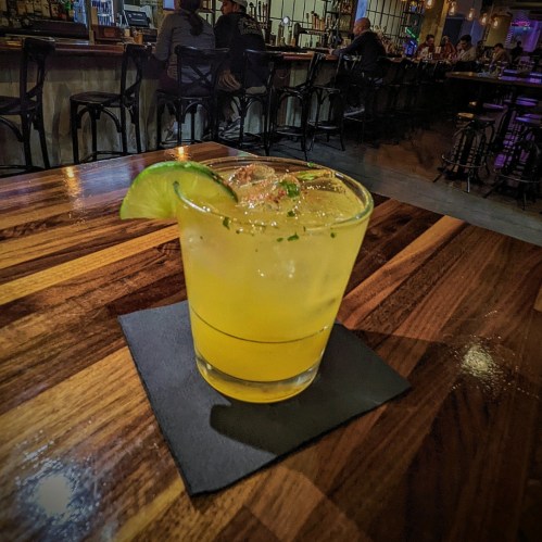 A refreshing cocktail with lime and mint sits on a wooden table in a dimly lit bar.