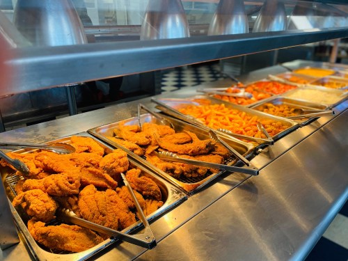 A buffet display featuring various trays of fried chicken, orange-colored snacks, and other food items.