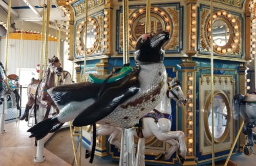 A whimsical carousel featuring a penguin-shaped ride, surrounded by ornate decorations and other animal figures.
