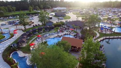 Aerial view of a vibrant pool area with cabanas, surrounded by trees and a parking lot filled with vehicles.