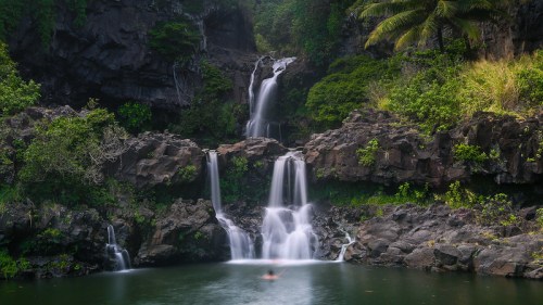 A serene waterfall cascades into a tranquil pool, surrounded by lush greenery and rocky cliffs.
