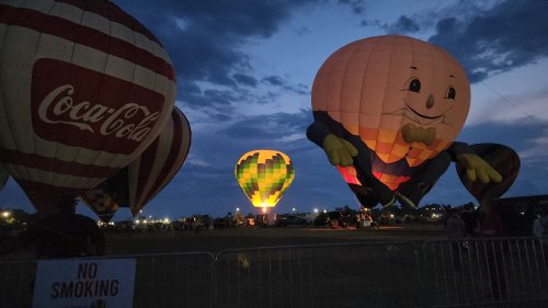 Colorful hot air balloons illuminated at dusk, with a large character balloon and a "No Smoking" sign in the foreground.