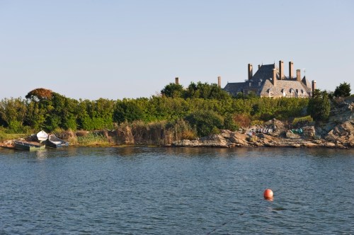 A serene waterfront scene featuring a house on a hill, surrounded by greenery and a small boat near the shore.