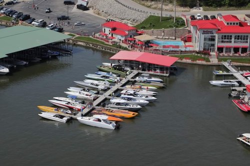 Aerial view of a marina with colorful boats docked at a pier near a red-roofed building.