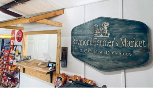Sign for "Raymond Farmer's Market" with a wooden design, featuring a counter and farm fresh produce theme.