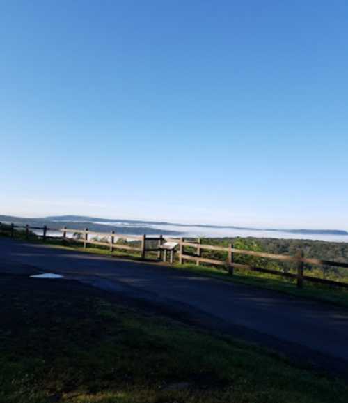 A scenic view of a foggy landscape with a wooden fence and clear blue sky in the background.