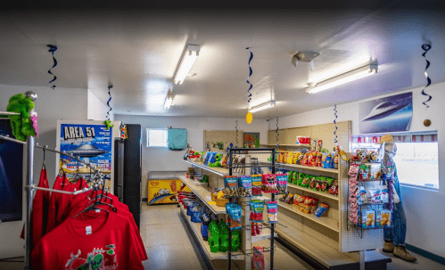 Interior of a small convenience store with shelves of snacks, drinks, and colorful decorations.